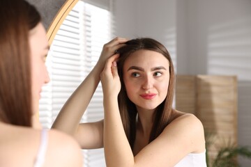 Naklejka premium Beautiful woman with healthy hair roots near mirror at home