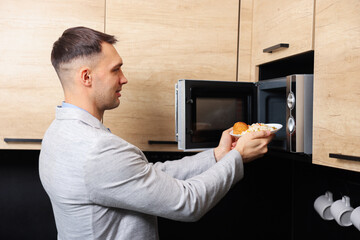 Man putting plate with lunch into microwave in kitchen