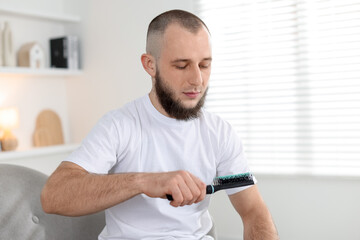 Baldness problem. Man with receding hairline holding brush at home