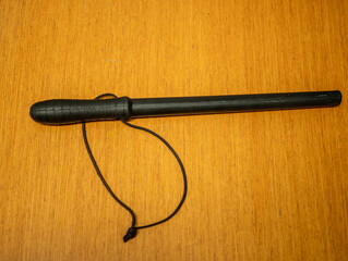 Black police baton with wrist strap placed on wooden surface, photographed from above.The baton is used by police officers as a means of coercion.