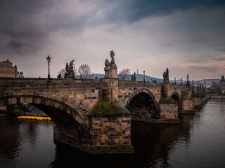 Fototapeta premium Charles Bridge in Prague during a moody evening with statues and arches reflected in the Vltava River, capturing a historic and romantic atmosphere.