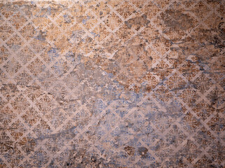 Old faded wallpaper with a vintage floral pattern in brown and blue tones, showing signs of age, wear, and peeling.