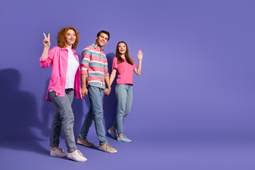Fototapeta premium Three cheerful friends walking hand in hand, gesturing carefree joy in casual attire against a vibrant purple background