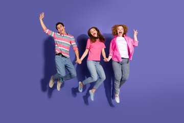 Fototapeta premium Three young friends jumping with joy against a vibrant purple background, showcasing youthful energy, happiness