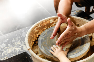 Making it together. Close-up of potter teaching child to make ceramic pot on the pottery wheel