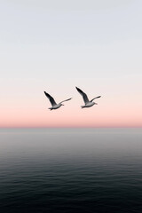 Two seagulls flying over calm ocean at pastel sunrise with minimalistic sky