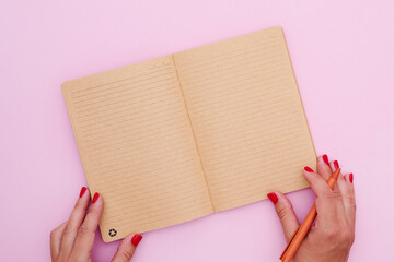 Female hand writing in an eco-conscious notebook on a lively pink backdrop, capturing the essence...