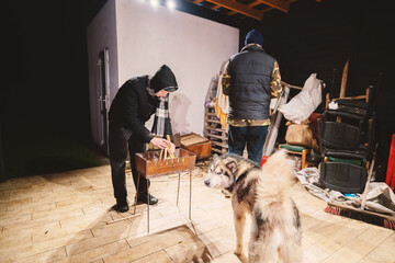 People setting up a fire pit with a dog in a cluttered backyard at night, ideal for outdoor...