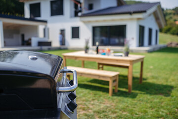 Backyard setup with barbecue grill and picnic table prepared for family gathering.