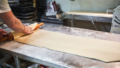 Rolling out pastry dough with wooden pin on floured table