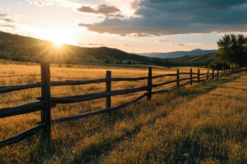 Fototapeta premium Sunset over a rural landscape with wooden fencing, golden grass, and a mountain in the distance.