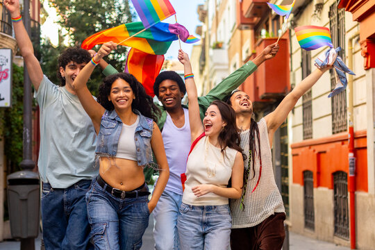 Happy multi ethnic friends waving rainbow flags celebrating gay pride in the city