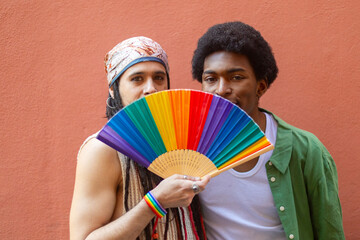 Obraz premium Gay couple hiding behind rainbow fan celebrating pride month