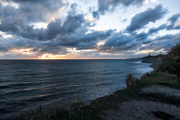 The sky is cloudy and the sun is setting. The ocean is calm and the water is dark blue