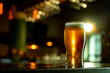 Tall pint of glowing amber beer with smooth foam top shining in warm pub light ambiance. Horizontal...