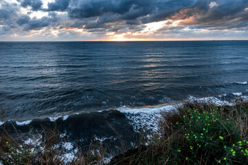The ocean is calm and the sky is cloudy. The sun is setting and the water is reflecting the colors of the sky
