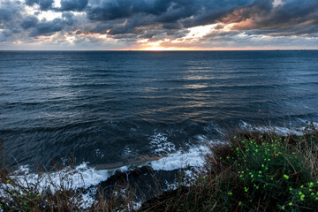 The ocean is calm and the sky is cloudy. The sun is setting and the water is reflecting the colors of the sky