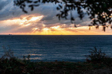 Gelendzhik resort. The sun is setting over the ocean, casting a warm glow on the water. The sky is filled with clouds, creating a moody atmosphere