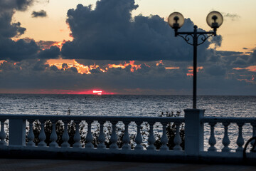 The sky is filled with clouds and the sun is setting. The water is calm and the sky is a beautiful orange color
