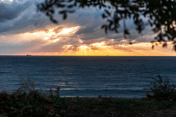 Gelendzhik resort. The sun is setting over the ocean, casting a warm glow on the water. The sky is filled with clouds, creating a moody atmosphere