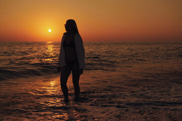 Female silhouette in soft evening glow, embracing freedom by sea. Gentle waves, warm colors, and...