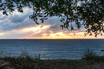 Gelendzhik resort. A beautiful sunset over the ocean with a tree in the background. The sky is filled with clouds and the sun is setting, creating a warm and peaceful atmosphere