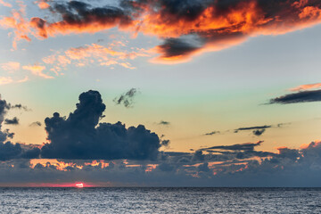 A beautiful sunset over the ocean with a large cloud in the sky. The sky is a mix of orange and blue colors