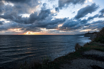 The sky is cloudy and the sun is setting. The ocean is calm and the water is dark blue