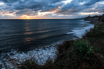 The sky is cloudy and the sun is setting. The ocean is calm and the water is dark blue