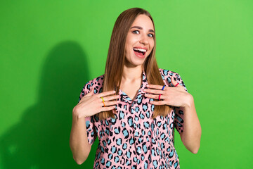 Cheerful young woman expressing surprise and excitement against a vivid green background wearing a...