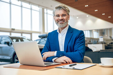 Man in car showroom wearing suit using laptop preparing sales agreement in business office