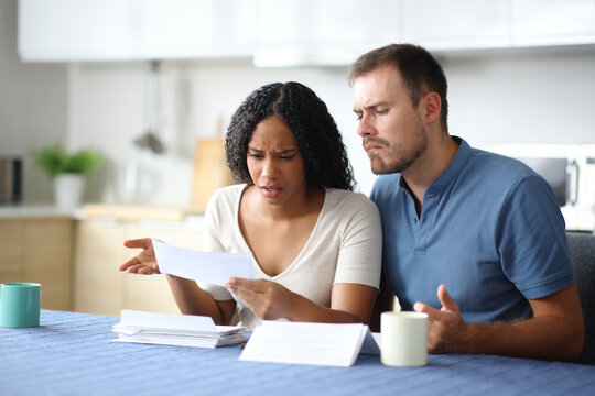 Angry interracial couple reading bank statement in the kitchen