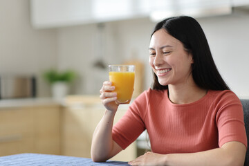 Happy asian woman drinking orange juice in the kitchen