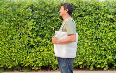 Side view shot of handsome man walking in the city with reusable white canvas bag