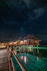 Luxury over water villas, bungalows with LED lights sea ocean with beach at night sunset time, Milky Way. Exotic adventure carefree travel vacation, summer resort landscape. Fantasy resort landscape