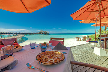 Luxury romantic sunny lunch table setup under umbrellas for couple in ocean view restaurant on tropical resort hotel outdoor restaurant with wine glasses and beautiful gourmet food. Vacation breakfast