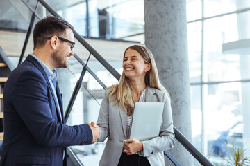 Two Business Professionals Smiling and Shaking Hands in Modern Office Setting