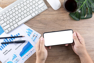 Obraz premium Top view of man's hand using smartphone with blank screen on wooden desk