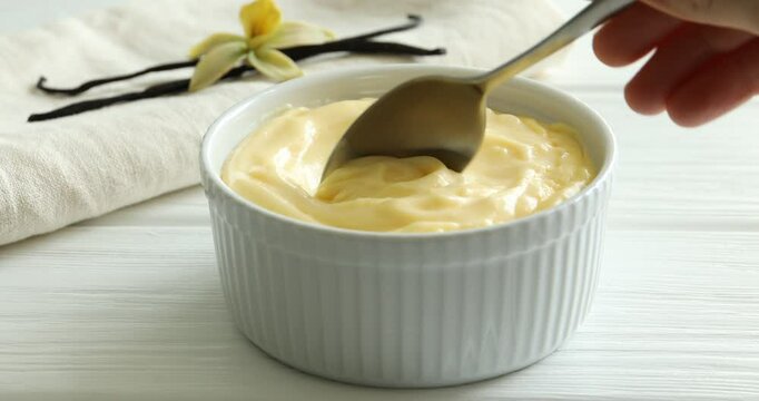 Woman eating delicious vanilla pudding at white wooden table, closeup