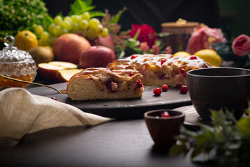 Ruddy yeast pie with filling on a dark table among fruits and flowers