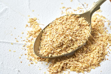 closeup pile of flake whole grain powder or wheat germ in steel spoon on white background with copy space