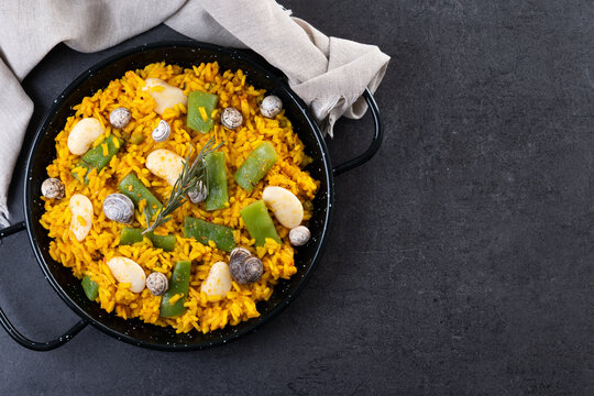 Traditional Valencian paella with rabbit, chicken, garrofon beans, snails, Moroccan green beans and saffron on black background. Top view. Copy space