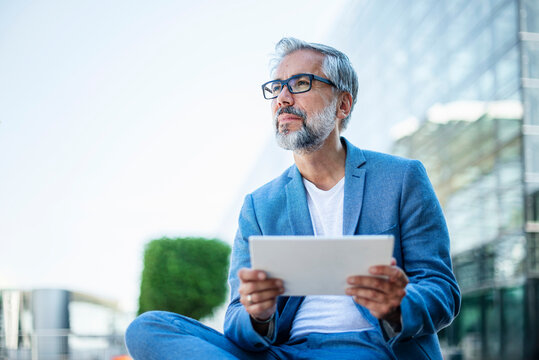 Businessman with tablet sitting outdoors in urban setting