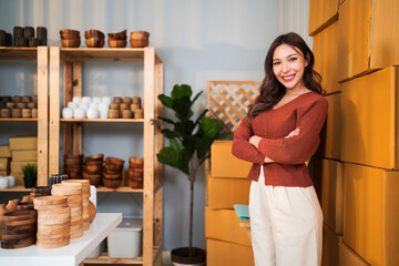 Confident female entrepreneur stands proudly in her small business studio surrounded by handmade craft products and shipping boxes, ready to grow her online store and brand presence.