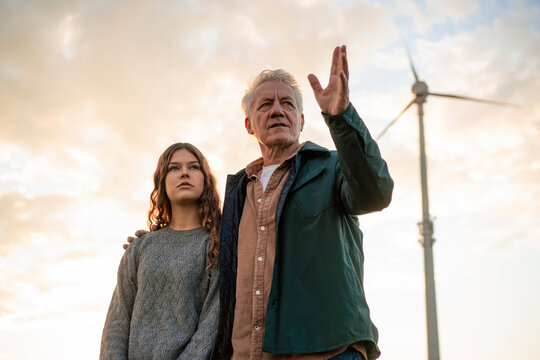 Grandfather and granddaughter discussing wind power outdoors at sunset