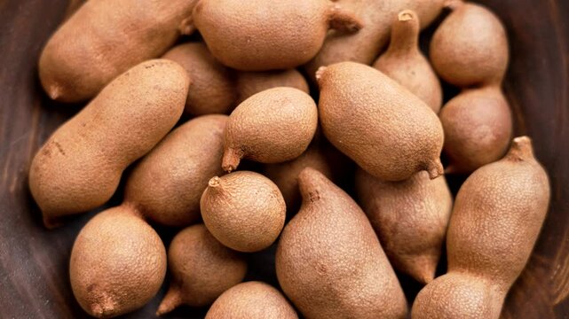 Tropical tamarind fruits in wooden bowl. Tamarindus indica pods. Top view. Rotation