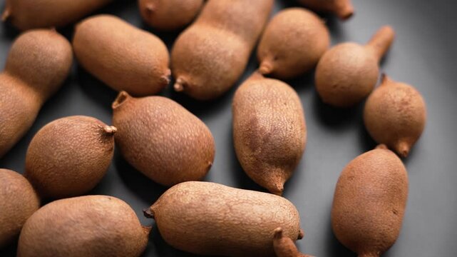 Shaking fresh tamarind fruits in shells on a black ceramic plate. Macro. Slow motion