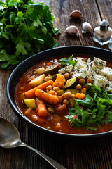 Fresh vegetable soup with chickpeas, feta cheese and cilantro on wooden table