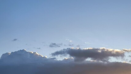 Blue cumulus clouds with orange tips change to a more orange color