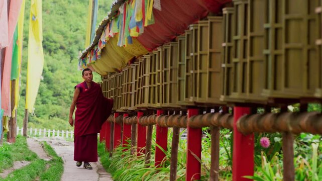 On the road to a temple on the hillside of Jiuzhaigou in Sichuan, a Tibetan monk in a crimson robe walks by and turns a long row of prayer wheels hung with colorful flags.